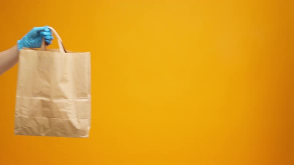 Courier in Gloves Passing Craft Shopping Bag with Delivery Against Yellow Background