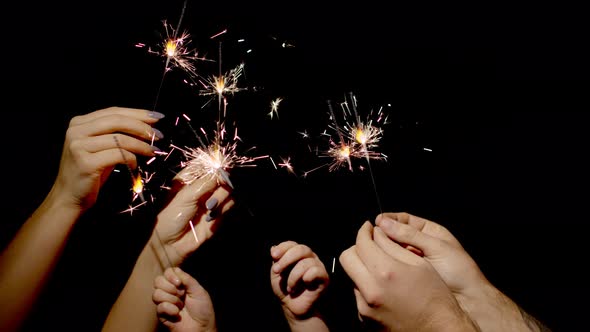 Close-up of Hands Holding and Waving Bengal Fire Burning Sparklers in Front of Black Background