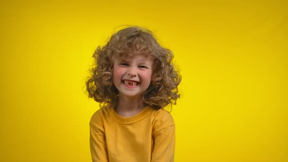 Cute Curly Girl with a Charming Toothless Smile is Smiling in a Yellow Studio