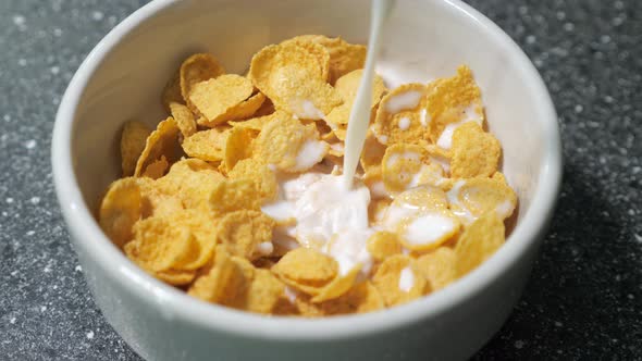 Pouring Milk in Bowl with Dry Cornflakes Preparing Breakfast.