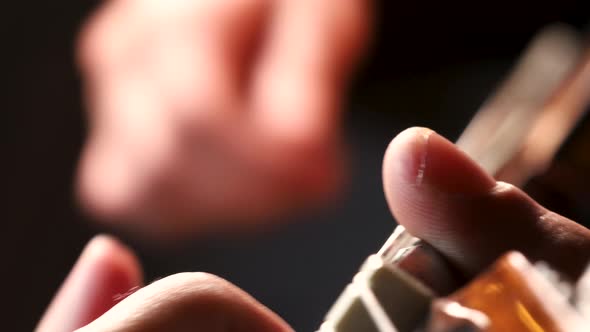 Macro shot of male hands playing acoustic guitar chords in dark room