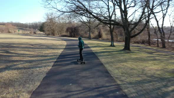 An aerial tracking of a man on an electric skateboard in an empty park on a sunny day. The drone fol