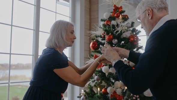 Grandparents Decorating Christmas Tree and Talking in Big and Bright House