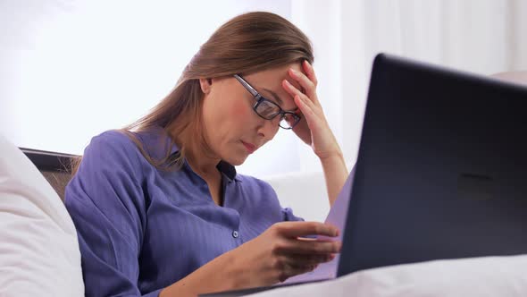 Young Woman with Laptop and Papers in Bed at Home