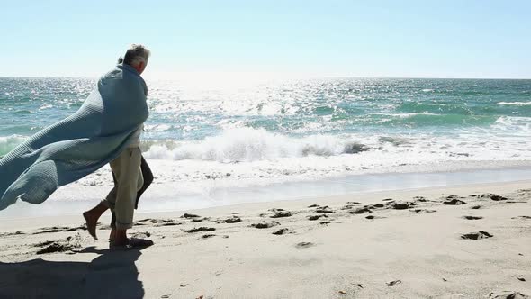 Mature couple walking on beach wrapped in blanket