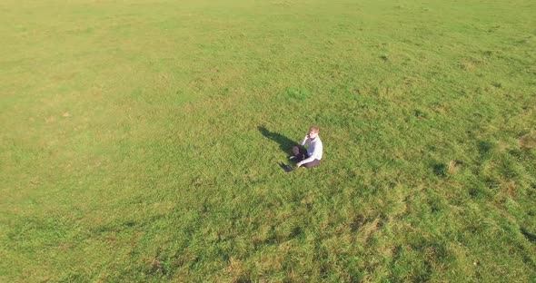 Low Orbital Flight Around Man on Green Grass with Notebook Pad at Yellow Rural Field