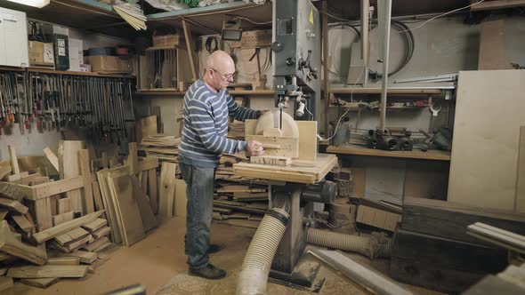 An Elderly Man in a Carpentry Workshop Saws Off the Remains of a Wooden Workpiece