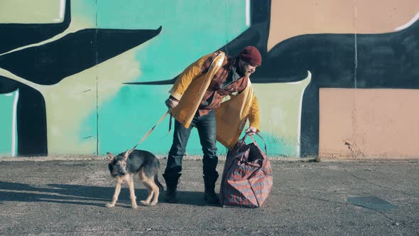 A Beggar is Standing Next to a Graffiti Wall with His Dog