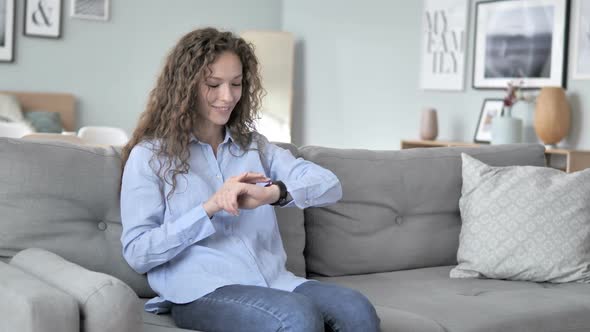 Curly Hair Woman Using Smartwatch While Sitting on Sofa