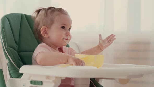 A Child Eats Porridge and Laughs While Sitting at a Table at Home