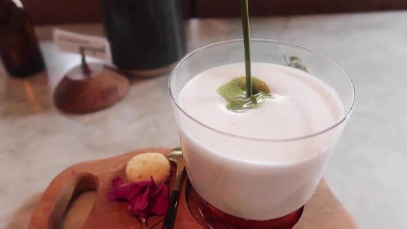 Pouring Matcha Green Tea into Creamy Coconut Milk Glass with Strawberry Jam in Circular Motion