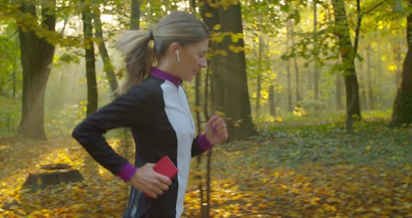 Young Attractive Woman Listening Music in the Earphone While Running in the City Park