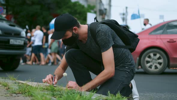 Male Protester Drawing Banner Sign in Hands with Marker in Rally Riot Crowd