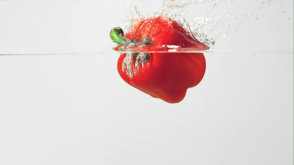 Super Slow Motion One Red Bell Pepper Falls Under the Water on a White Background
