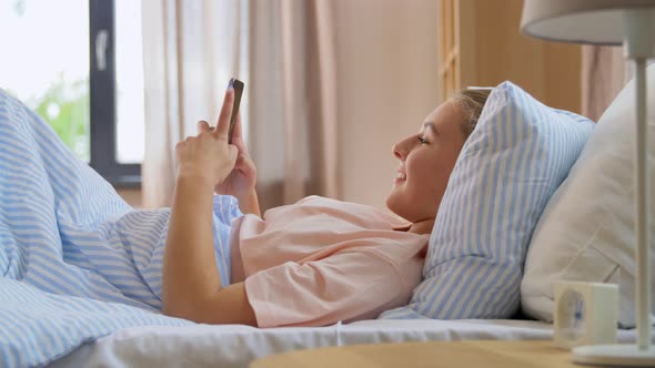 Happy Girl with Smartphone in Bed at Home