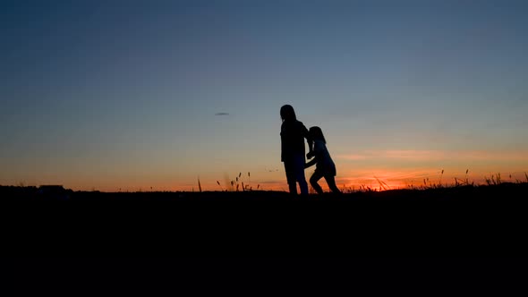 Happy family mom and daughter little girl play in the meadow at sunset. Mom and a child in a summer