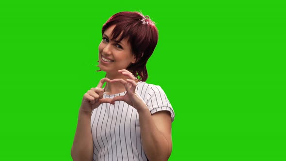 Portrait of cute brunette woman posing on green screen performing heart gesture