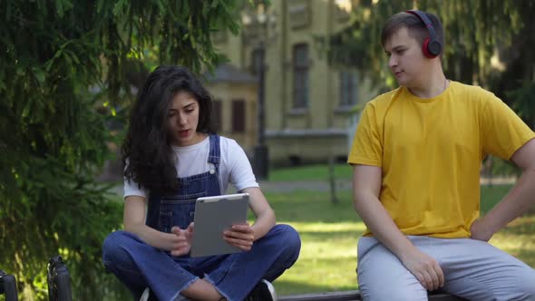 Focused Slim Beautiful Woman Studying with Tablet As Relaxed Careless Man Dancing Sitting on Bench