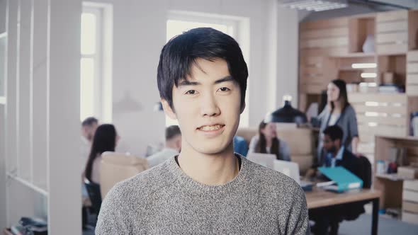 Portrait of Young Successful Asian Businessman Smiling at Busy Office. Handsome Male Manager Looking