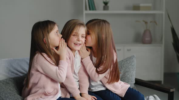 Three Sisters Triplets Identical Same Little Girls Children Sitting on Couch at Home in Living Room