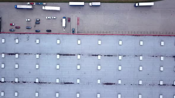 Moving Aerial Side Shot of Industrial Warehouse Loading Dock where Many Truck with Semi Trailers Loa