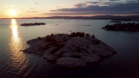 Rocky Granite Island with Pine Trees in Blue Lake at Sunset, Drone Aerial Wide Orbit Pan. Flying ove
