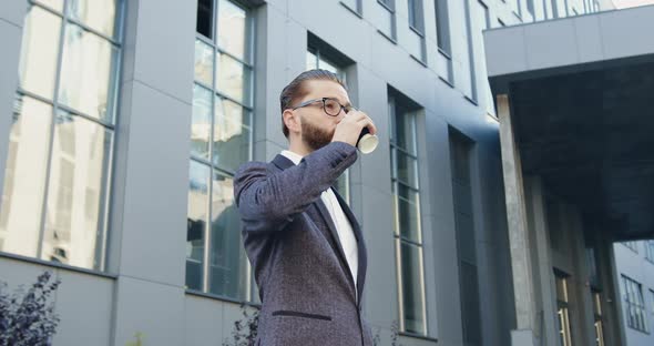 Businessman Drinking Coffee Near Office Building and Checking Time while