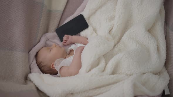 Top View Wide Shot Sleeping Infant Lying in Bed with Smartphone