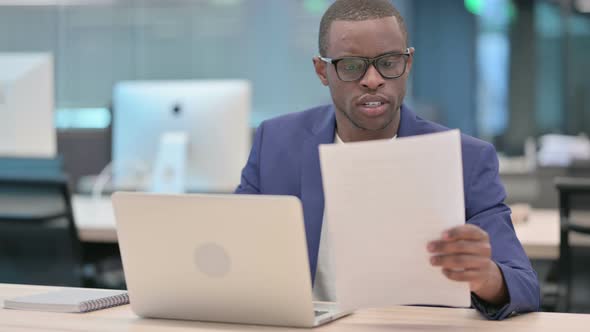 Businessman with Laptop Having Loss Reading Documents