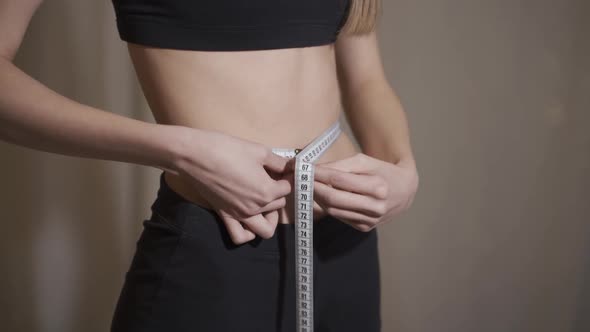 Side View of Young Woman Measuring Her Waist with Measure Tape