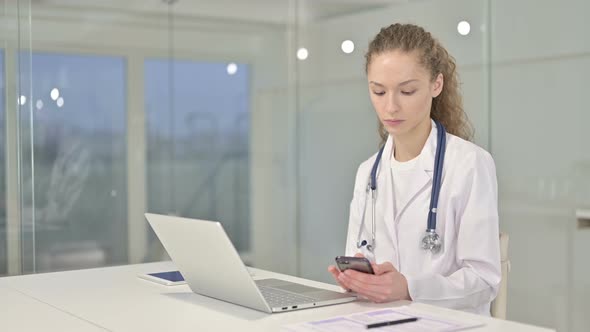 Professional Young Female Doctor Using Smartphone in Office 