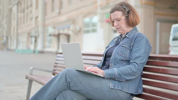 Busy Old Woman Using Laptop Sitting Outdoor on Bench