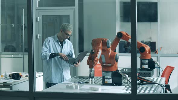 Male Lab Worker is Supervising an Experiment with a Robotic Device