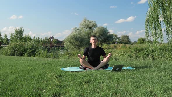 Man practicing yoga, meditating in park, sitting in lotus pose on yoga mat