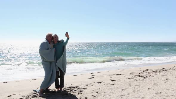 Mature couple on beach with blanket, taking a picture of themselves