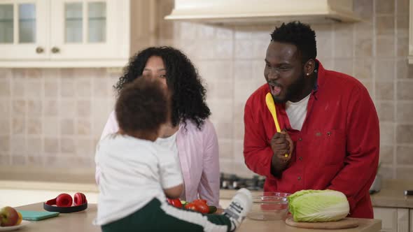 Relaxed Couple of African American Parents Singing Dancing in Kitchen with Toddler Boy Sitting on