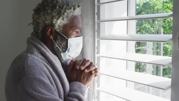 Senior man wearing face mask looking out of window at home
