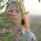 A Little Girl with a Sad Face Looks through the Branches of a Leafy Tree - VideoHive Item for Sale