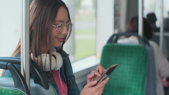 Young Stylish Woman Using Public Transport, Sitting with Phone and Headphones in the Modern Tram.