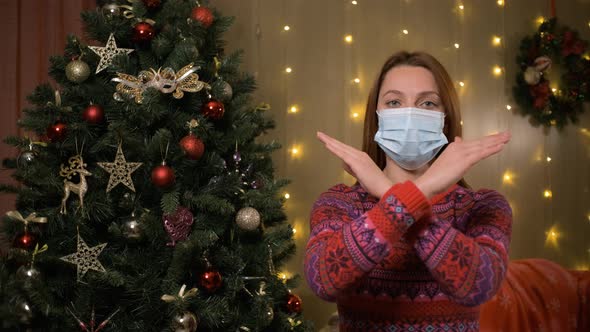 Female in Face Mask Looks in Camera Standing Next to Decorated Christmas Tree