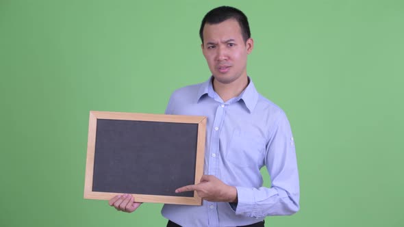 Stressed Asian Businessman Holding Blackboard and Giving Thumbs Down