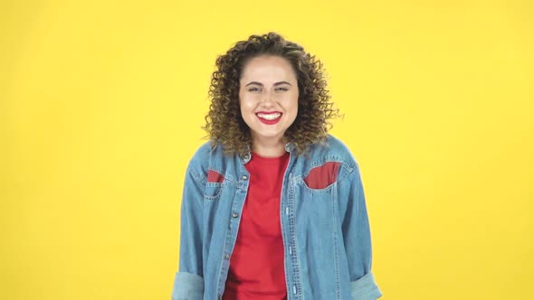 Lovely Curly Girl Smiles Broadly and Winks on Yellow Background at Studio, Slow Motion