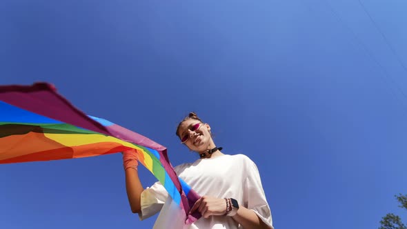 A Young Woman Develops a Rainbow Flag Against the Sky