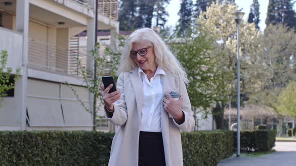 Mature businesswoman standing in city, using smartphone