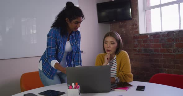 Diverse female business colleagues in discussion at work looking at laptop