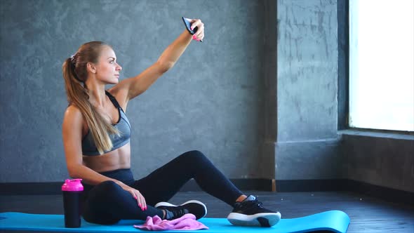 A Young Girl with a Good Figure Makes Selfie on a Mobile Phone in the Gym