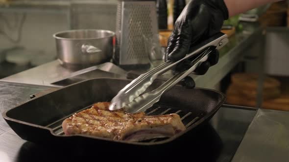 Closeup of a Chef Frying a Pork Steak on a Grill Pan in the Restaurant Kitchen