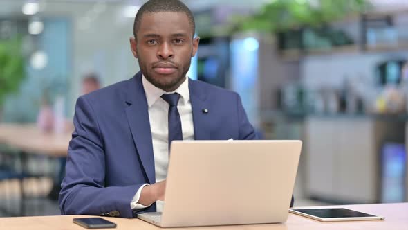 African Businessman with Laptop Doing Thumbs Down in Office