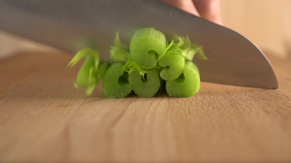 A cook cuts celery with a knife on a wooden surface.