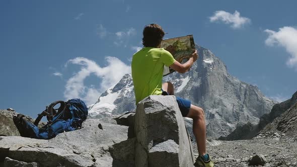 Tourist Hiker Man Studies a Map and Explores a Route in the Mountains, Sitting on a Rock, Slow